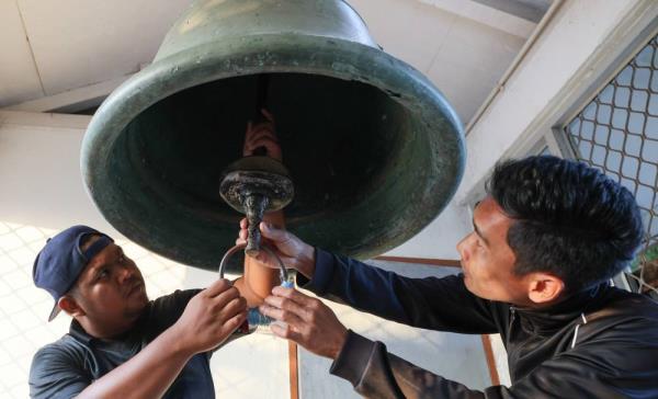 Muhammad Muizzuddin Mansor, 25, (right), assisted by his cousin Muhammad Hamidi Aminudin, 30, who was tasked with ringing the large bell, inspects the bell before ringing it at Bukit Puteri. - Photo by Bernama 